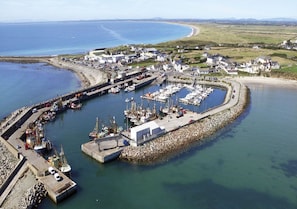 Vue aérienne d’une marina côtière, avec des bateaux amarrés, un petit quai et une digue rocheuse.