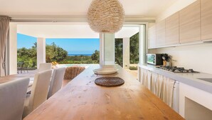A modern kitchen with a wooden table, wicker baskets, and a view of the sea. - Villa Lisy by Perle di Puglia (Carovigno)