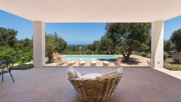 A covered patio with a wicker chair, a pool, and lounge chairs. - Villa Lisy by Perle di Puglia (Carovigno)