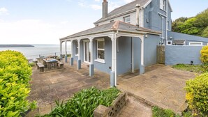 A coastal house with a covered patio, a view of the sea, and a garden area.