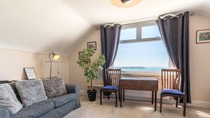 A cozy room with a sofa, two chairs, a small table, a potted plant, and a window with curtains.