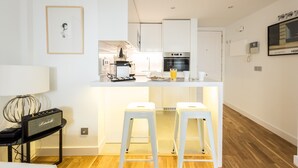 A modern kitchen with white cabinets, a built-in oven, and a bar area with stools. - Latina Suite (Madrid)