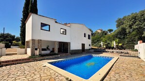 A modern house with a swimming pool, stone patio, and a view of a hill with trees. - Villa Castell - Urb Mas Pere (Calonge)