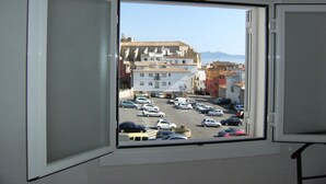 Une fenêtre donnant sur un parking et sur des bâtiments situés au loin.