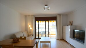 Un salon moderne comprenant un canapé, une table à manger, des chaises, un téléviseur et un balcon avec des rideaux.