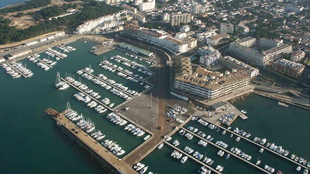 Vue aérienne d’une marina où sont amarrés de nombreux bateaux, entourée d’immeubles résidentiels et, au loin, d’un paysage vallonné.