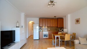 Un appartement moderne comprenant un salon, un coin repas, une cuisine et un téléviseur posé sur un meuble blanc.