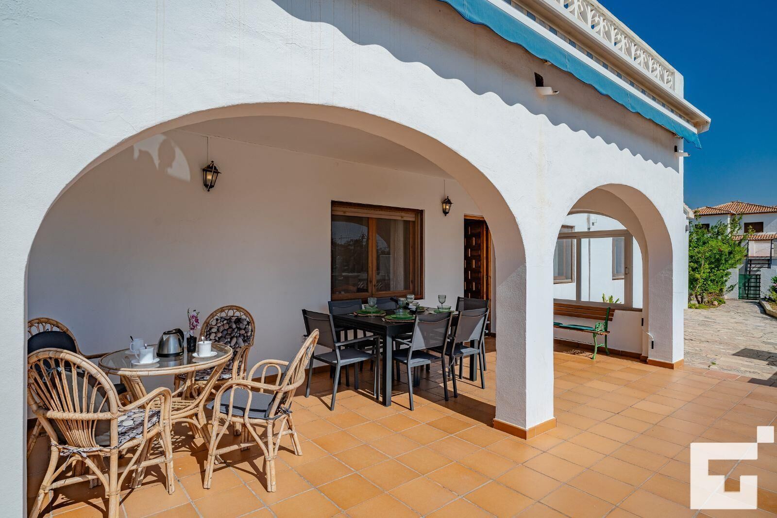 Un patio cubierto con mesa y sillas de comedor, un pequeño espacio de descanso y vistas al paisaje circundante.