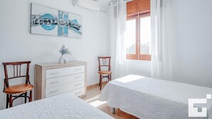 A room with two beds, a wooden dresser, a chair, a painting, and a window with curtains. - Benicolada - Grupo Turis - Calpe, Costa Blanca (Calpe)