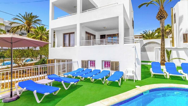 A two-story building with a pool, blue lounge chairs, and palm trees. - Villa Pou Uno - Five Bedroom Villa, Sleeps 10 (Cala d'Or)