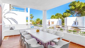 A terrace with a white table and chairs, a flower vase, and a view of white buildings and trees. - Villa Pou Uno - Five Bedroom Villa, Sleeps 10 (Cala d'Or)