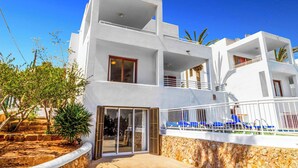 A modern white building with multiple balconies, a pool area with blue lounge chairs, and a stone retaining wall. - Villa Pou Uno - Five Bedroom Villa, Sleeps 10 (Cala d'Or)