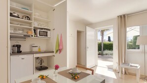 A modern kitchen with white cabinets, a microwave, and a coffee maker. There is a dining table with a white cup and saucer, and a small vase with flowers. - GUESTHOUSE PALMA - ADULTS ONLY (Palma de Mallorca)