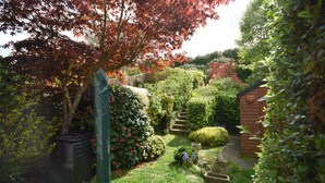 Un jardin où l’on trouve une grande variété de plantes, un abri en bois et un chemin pavé de pierres.