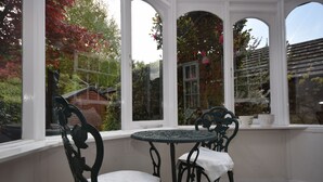 Une véranda avec une table ronde et deux chaises, de grandes fenêtres et une vue sur un jardin.