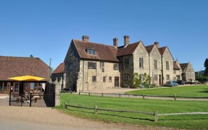 A large stone building with multiple chimneys, a paved driveway, and a grassy area in front. - Cosy holiday home in a quiet area of Midhurst, West Sussex. (Midhurst)