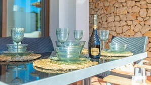 Une table à manger avec de la vaisselle en verre et une bouteille, disposée sur des sets de table en fibres tressées, avec un mur en pierre et une fenêtre en arrière-plan.