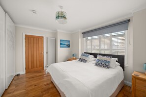Een slaapkamer met een groot bed, een houten deur, een radiator, een schilderij en een raam met zonwering.