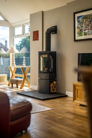 Een moderne woonkamer met een zwart houtvuuroven, een glazen tafel met een lamp en een lijst met een afbeelding aan de muur.