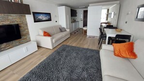 Een moderne woonkamer met een flatscreen televisie, een bank en een eethoek met een tafel en stoelen.