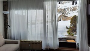 Een kamer met uitzicht op een besneeuwde berg, een radiator en een stoel.