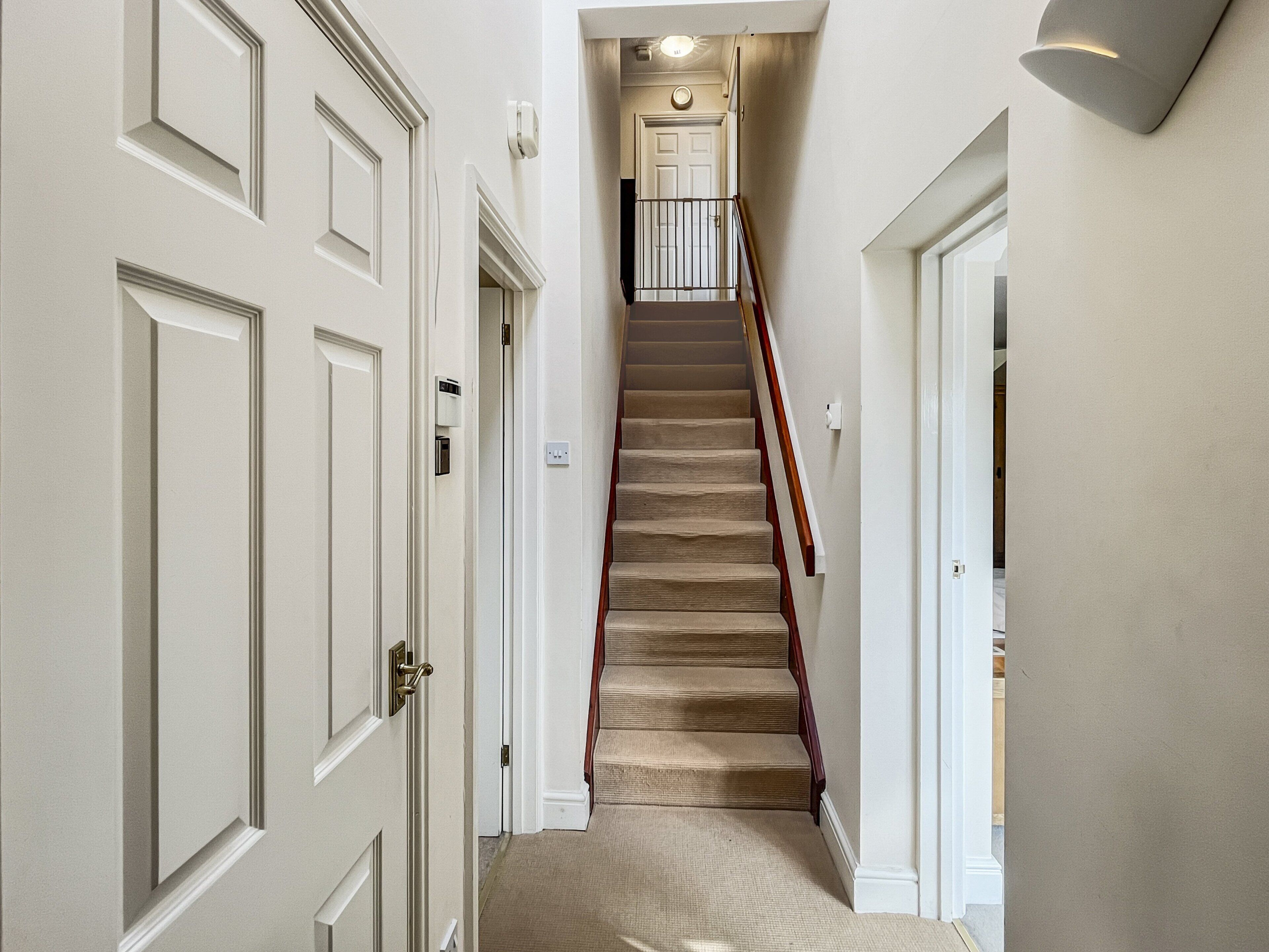 Un pasillo con una escalera alfombrada, puertas blancas y una lámpara en la pared.