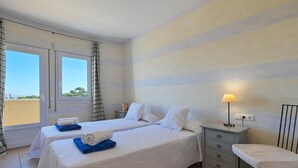 A hotel room with two beds, a small bedside table with a lamp, a chair, and a view of the outdoors.