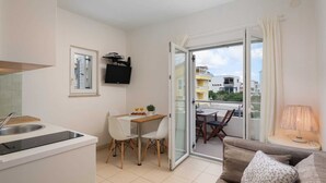 Un espacio habitable compacto con kitchenette, comedor y balcón con vistas al vecindario.
