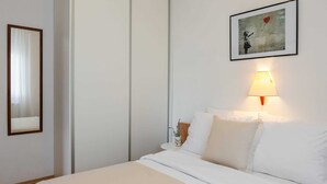 Habitación de hotel con cama, lámpara de noche, un cuadro en la pared y un espejo.