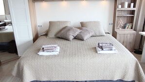 A neatly made bed with a textured beige duvet, two pillows, and folded towels on the bed.