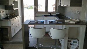 A modern kitchen with a central island, two white bar stools, and a view of the city through large windows.