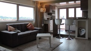 A modern living room with a sofa, a coffee table, and a dining area with a chair and a lamp.
