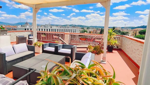 A rooftop terrace with outdoor furniture, potted plants, and a view of the cityscape.