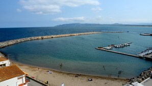 Vista sulla costa con spiaggia sabbiosa, frangiflutti rocciosi e acque calme.