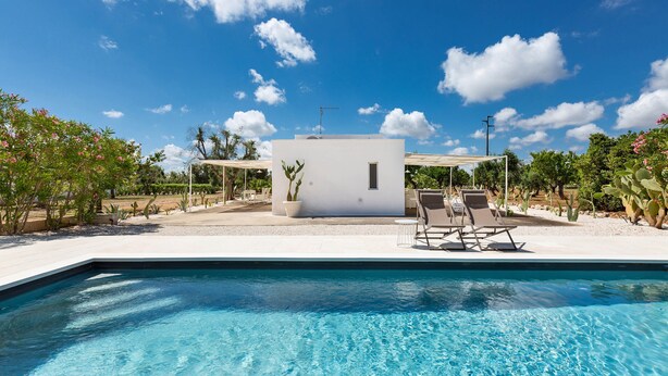 A swimming pool with lounge chairs and a small building with a cross on top, surrounded by greenery.