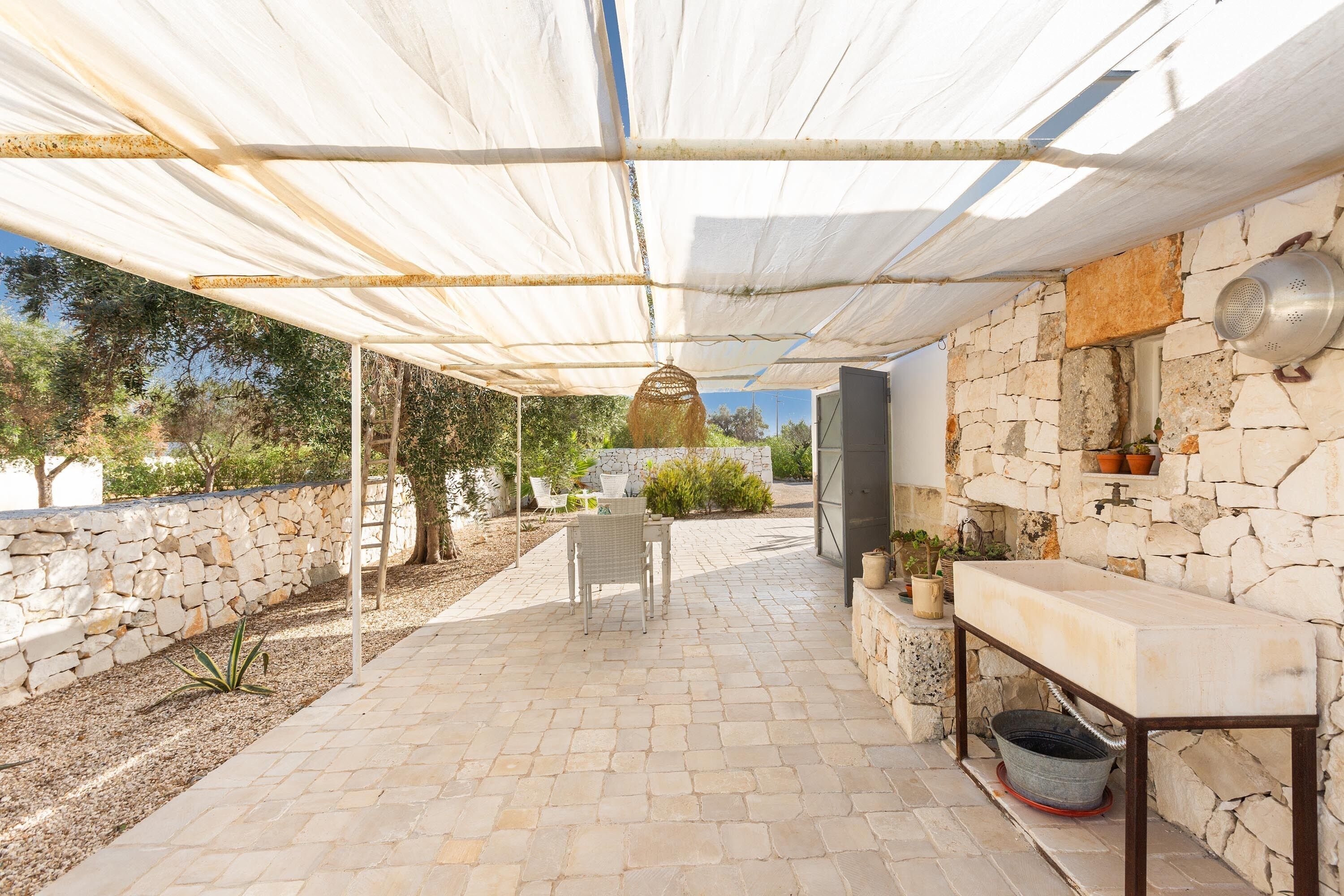 An outdoor patio with stone flooring, a table, chairs, and a hanging light fixture.