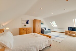 Une chambre à coucher comprenant un lit, une commode en bois, une armoire, un canapé, un meuble pour la télévision et une lucarne.