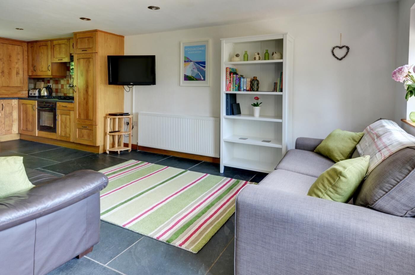 Ein modernes Wohnzimmer mit einem grauen Sofa, einem Streifen Teppich, einem Fernseher, einem Bücherregal und Holz Küchenschränken.