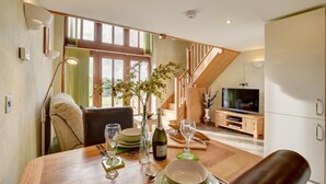 A dining area with a wooden table set for two, a television, and a staircase leading to an upper level.