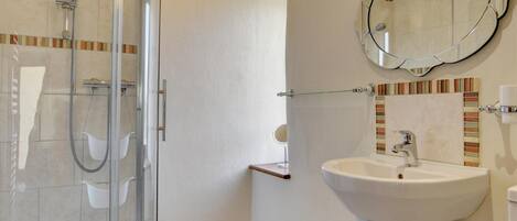 Een moderne badkamer met een douche met glazen wand, een wastafel op een voetstuk en een spiegel met decoratieve lijst.