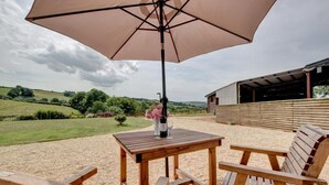 An outdoor seating area with a table and chairs, a large umbrella, and a view of a rural landscape.