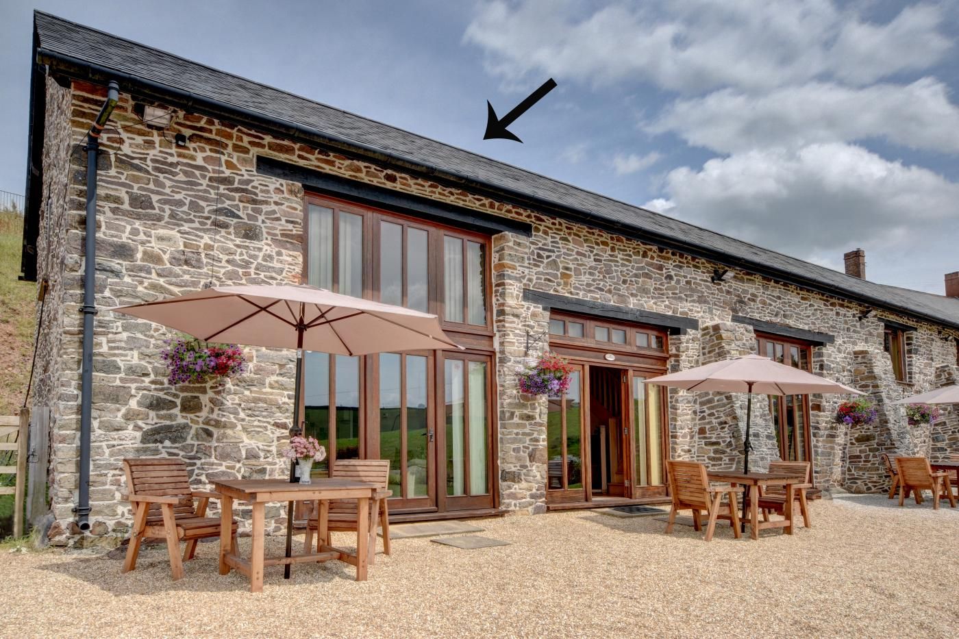 A stone building with a large wooden table and chairs, outdoor umbrellas, and flower baskets.