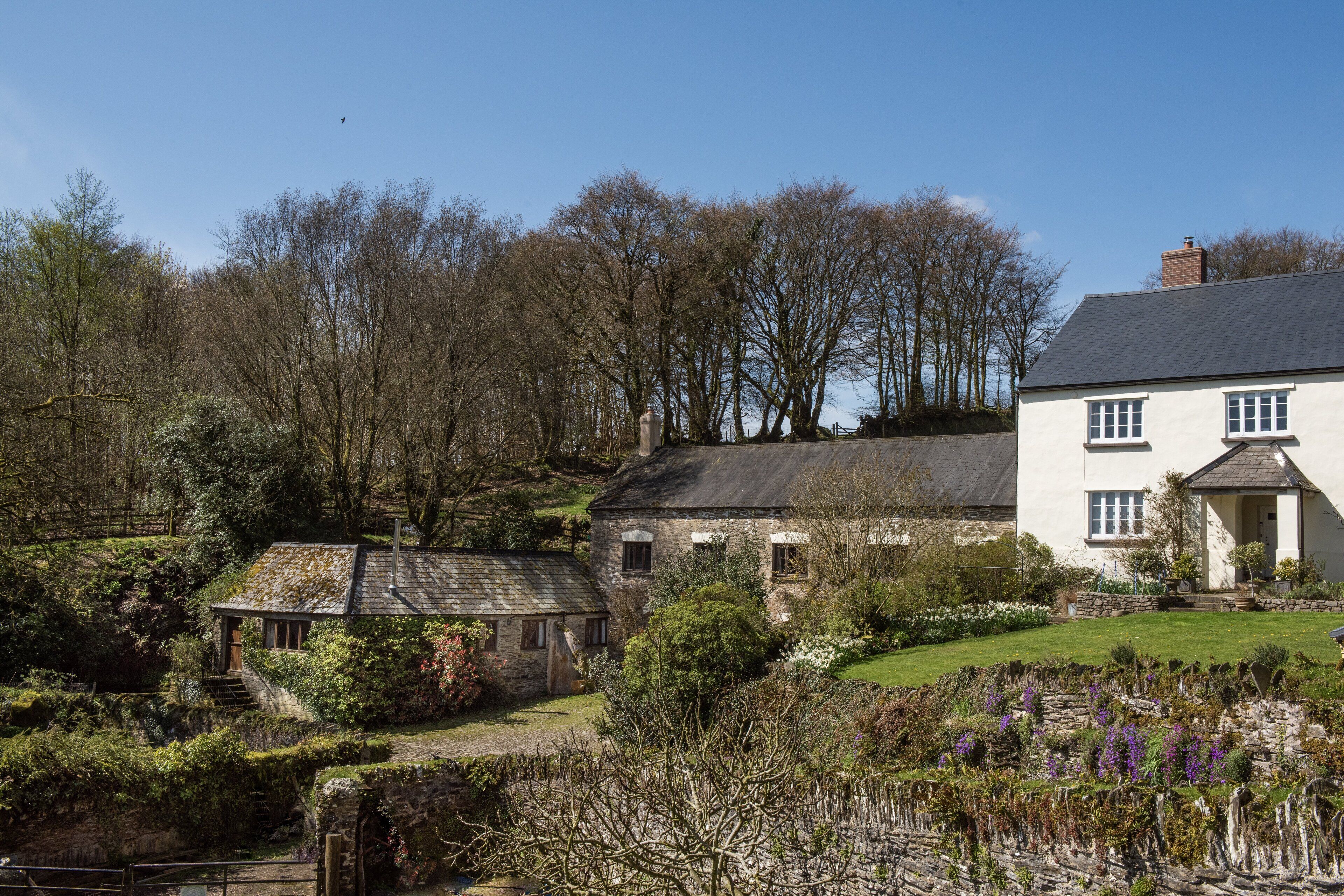 A traditional stone house with a garden, a small adjacent structure, and a clear blue sky.