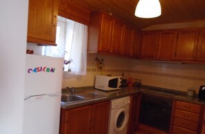 Kitchen with a refrigerator, microwave, and washing machine, featuring a tiled backsplash and window.