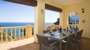 Un coin repas avec une table dressée pour six personnes, offrant une vue panoramique sur la mer.