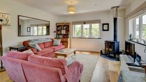 A cozy living room with a pink sofa, a wooden bookshelf, a fireplace, and large windows. - Linhay Cottage, Withypool (Withypool)