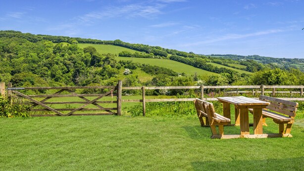 A picnic table and bench in a grassy field with a wooden fence and a view of rolling hills. - Linhay Cottage, Withypool (Withypool)