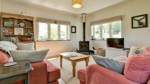A cozy living room with a sofa, a coffee table, a bookshelf, and a fireplace. - Linhay Cottage, Withypool (Withypool)