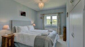 A bedroom with a bed, bedside lamps, a wooden nightstand, a window with curtains, and a view of greenery outside. - Linhay Cottage, Withypool (Withypool)