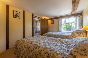 A bedroom with two beds, a wooden door, a window with curtains, and a radiator.